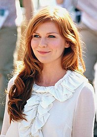 A red-headed woman smiles while wearing a white top with frill detailing.